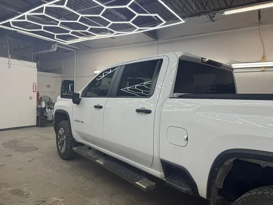 White Chevy Silverado HD pickup with tinted windows in a shop